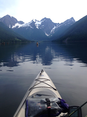 Beautiful photo of a kayak fishing in the foreground with calm water and gorgeous mountains reflected in the distance
